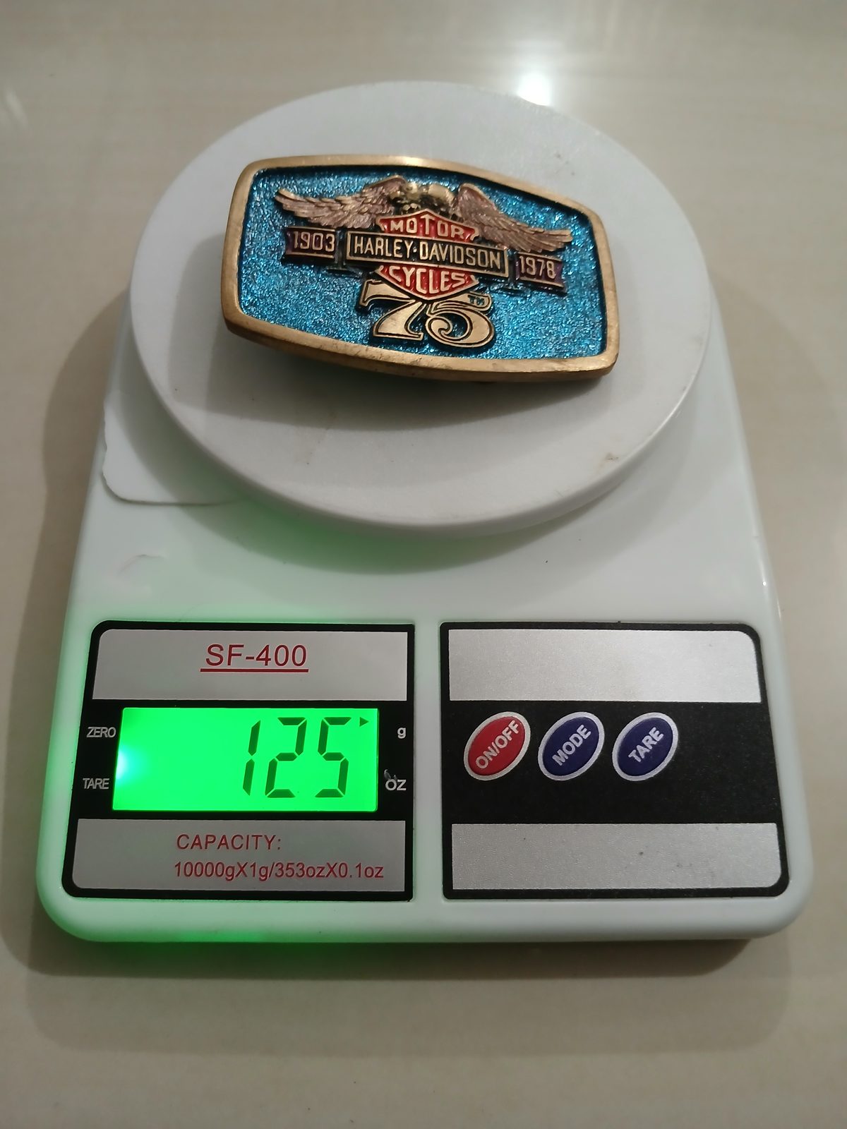 Harley-Davidson 75th Anniversary 1903-1978 Vintage Belt Buckle – On scale showing weight Harley-Davidson 75th Anniversary 1903-1978 vintage belt buckle – on scale showing weight